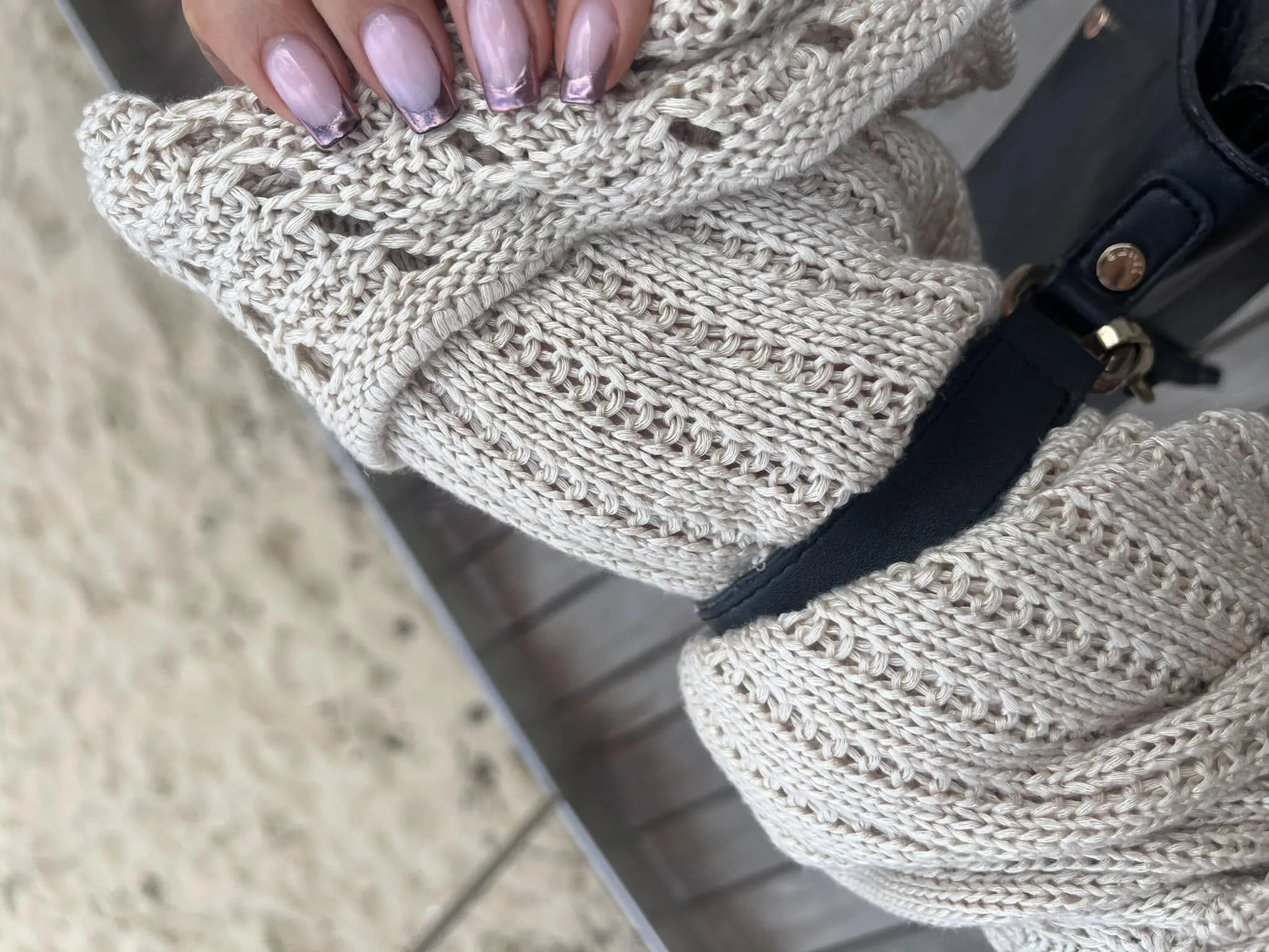 Close-up of long coffin nails in a pink-pearl to rose-chrome ombre finish, resting on cream cable-knit